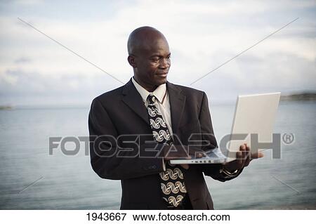 A Businessman Using A Laptop Computer By The Water's Edge; South Caicos Turks And Caicos Islands View Large Photo Image Stock Photo - A Businessman Using A Laptop Computer By The Water's Edge; South Caicos Turks And Caicos Islands. Fotosearch
