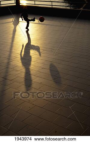 Picture - A Child Kicks A Ball And Has A Large Shadow At Sunset; Camogli Liguria Italy. Fotosearch