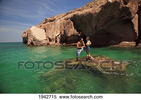 Stock Photography - A Father And Son Standing On A Rock In The Ocean At Los Islotes National Marine Park Espiritu Santo Island; La Paz Baja California Mexico. Fotosearch