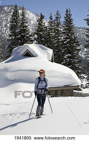 Stock Photography - A Female Snowshoeing With A Building Covered In Snow In The Background; Waterton Alberta Canada. Fotosearch