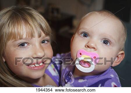 Picture - a girl holding a baby with a pacifier; moraga california united states of america. Fotosearch
