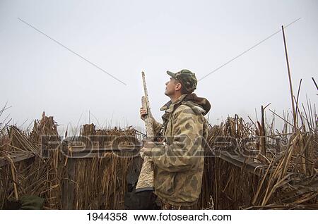 Stock Photo - a hunter in blind wearing camouflage and holding a rifle; colusa california united states of america. Fotosearch