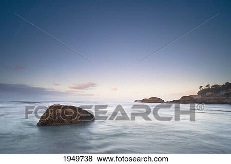 Stock Photo - a large rock in the water by the coastline at sunset; cape foulwind new zealand. Fotosearch