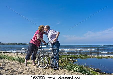 Stock Image - a man and woman exchange a kiss while on a bike ride along the water; northumberland england. Fotosearch