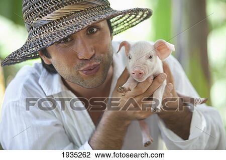 Stock Image - A Man Holds A Baby Pig; Island Of Bohol, Philippines. Fotosearch