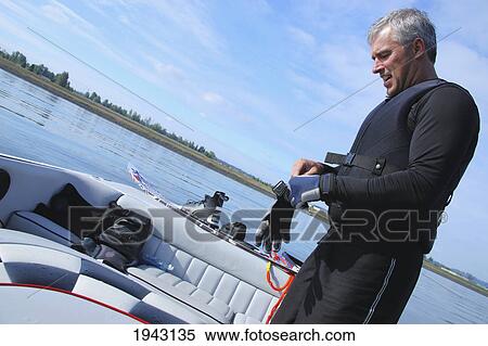 Stock Photography - A Man In A Boat Putting On Water Skiing Gloves; Troutdale Oregon United States Of America. Fotosearch