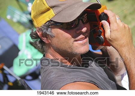 Stock Photograph - A Man Listening To A Sporting Event On An Orange Radio; Troutdale Oregon United States Of America. Fotosearch