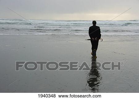 Stock Photo - A Man On A Wet Beach Holding An Umbrella; Tofino British Columbia Canada. Fotosearch