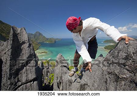 Picture - A Man Rock Climbs On Top Of Sharp Limestone Spires Overlooking The Village Of El Nido; El Nido, Bacuit Archipelago, Palawan, Philippines. Fotosearch