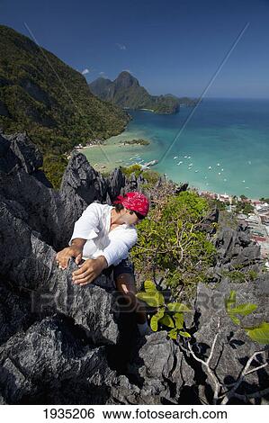 A Man Rock Climbs On Top Of Sharp Limestone Spires Overlooking The Village Of El Nido; El Nido, Bacuit Archipelago, Palawan, Philippines View Large Photo Image Stock Photograph - A Man Rock Climbs On Top Of Sharp Limestone Spires Overlooking The Village Of El Nido; El Nido, Bacuit Archipelago, Palawan, Philippines. Fotosearch
