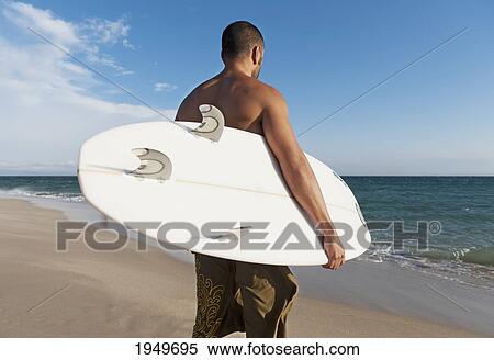 a man standing on the beach holding his surfboard; tarifa cadiz andalusia spain View Large Photo Image Stock Photography - a man standing on the beach holding his surfboard; tarifa cadiz andalusia spain. Fotosearch