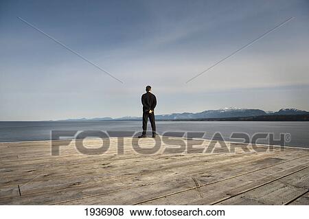 A Man Stands At The End Of A Wooden Dock Looking Out Over The Ocean; Chrome Island British Columbia Canada View Large Photo Image Stock Photo - A Man Stands At The End Of A Wooden Dock Looking Out Over The Ocean; Chrome Island British Columbia Canada. Fotosearch