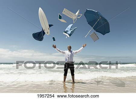 a man stands in the ocean with items from work and vacation flying over his head; tarifa cadiz andalusia spain View Large Photo Image Picture - a man stands in the ocean with items from work and vacation flying over his head; tarifa cadiz andalusia spain. Fotosearch