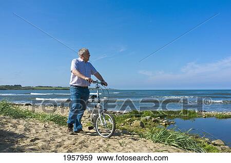 Stock Photo - a man with his bicycle on the beach along the coast; northumberland england. Fotosearch