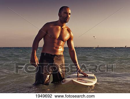 Stock Image - a man with his surfboard in the water at sunset; tarifa cadiz andalusia spain. Fotosearch