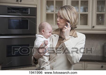 A Mother Holding A Baby While Taking On The Phone; Jordan Ontario Canada View Large Photo Image Stock Photograph - A Mother Holding A Baby While Taking On The Phone; Jordan Ontario Canada. Fotosearch