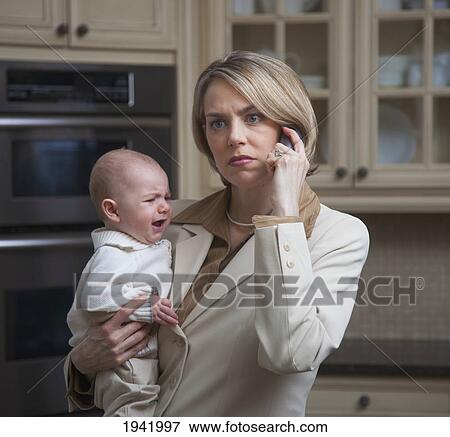 Stock Photo - A Mother Holding Her Crying Baby With A Worried Look While Talking On The Phone; Jordan Ontario Canada. Fotosearch