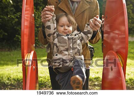 Stock Photograph - a parent holds a young child's hands as they climb a playground structure; thomastown county kilkenny ireland. Fotosearch