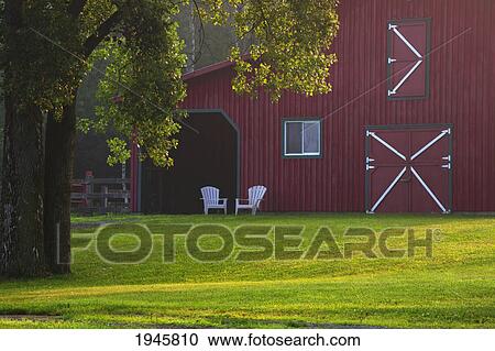 Stock Image - a red barn with two adirondack chairs in front; iron hill quebec canada. Fotosearch