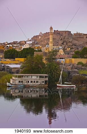Stock Image - A Sailboat On The River's Edge With A View Of The Village At Dusk; Nubia Egypt. Fotosearch