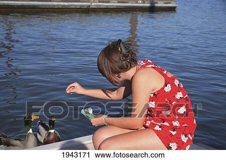 Stock Image - A Teenage Girl Feeds Ducks Off A Boat Dock; Portland Oregon United States Of America. Fotosearch