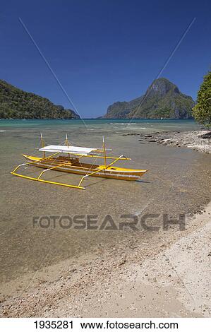 Stock Image - A Tradional Wooden Bangka Boat Sits In The Picturesque And Scenic Bay; El Nido, Bacuit Archipelago, Palawan, Philippines. Fotosearch
