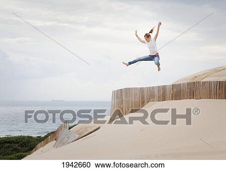 Stock Image - A Woman Jumps Over A Fence In The Punta Paloma Sand Dunes; Tarifa Cadiz Andalusia Spain. Fotosearch
