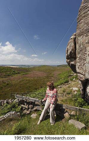 Stock Image - a woman leans on a wooden rail looking out at the landscape; northumberland england. Fotosearch