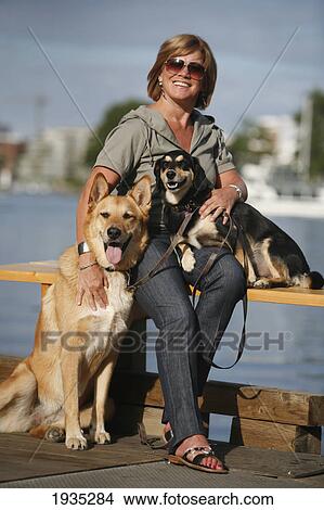 Picture - A Woman Sits With And Holds Her Pet Dogs In Victoria's Inner Harbour; Victoria, British Columbia, Canada. Fotosearch