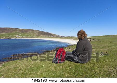 Stock Image - A Woman Sits With Her Backpack Looking Out Over The Coastline; Noss Scotland. Fotosearch