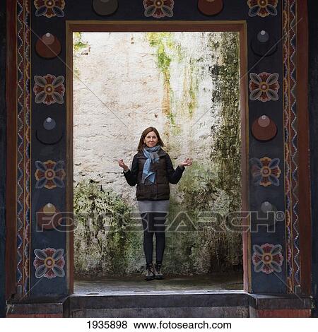 Stock Photo - A Woman Stands Against A Wall In An Ornate Doorway Of Trongsa Dzong; Trongsa, Trongsa District, Bhutan. Fotosearch
