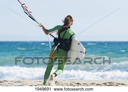 Stock Image - a woman with her kitesurfing board walking into the water; tarifa cadiz andalusia spain. Fotosearch