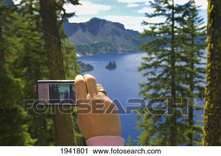 Stock Image - A Woman's Hand Taking A Scenic Picture With Her Camera; Crater Lake Oregon United States Of America. Fotosearch