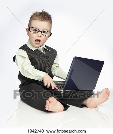 Stock Image - A Young Boy Wearing A Suit And Eyeglasses Using A Laptop Computer; Edmonton Alberta Canada. Fotosearch