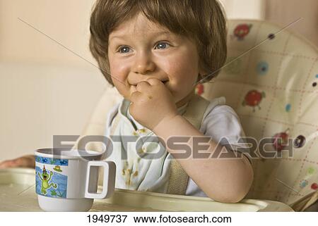 Stock Photo - a young child eats a snack in a highchair; thomastown county kilkenny ireland. Fotosearch