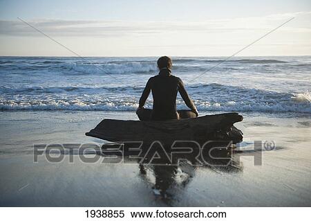 Stock Photography - A Young Man Sits On A Piece Of Driftwood Looking Out At The Ocean; La Push Washington United States Of America. Fotosearch