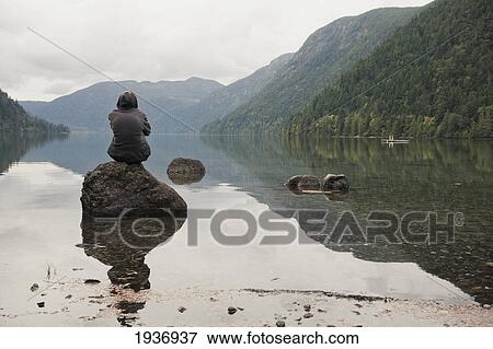 A Young Man Sits On A Rock In Cameron Lake; British Columbia Canada View Large Photo Image Stock Photo - A Young Man Sits On A Rock In Cameron Lake; British Columbia Canada. Fotosearch