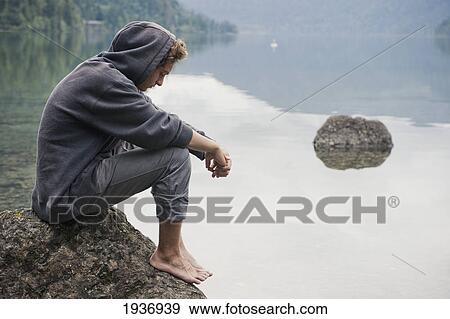 A Young Man Sits On A Rock In Cameron Lake; British Columbia Canada View Large Photo Image Stock Photo - A Young Man Sits On A Rock In Cameron Lake; British Columbia Canada. Fotosearch