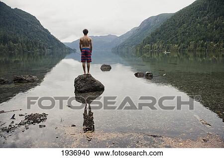 Stock Image - A Young Man Stands On A Rock In Cameron Lake; British Columbia Canada. Fotosearch