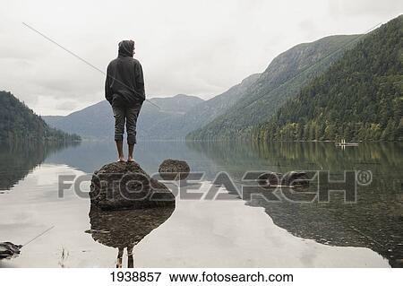 Stock Photo - A Young Man Stands On A Rock Looking Out Over Cameron Lake; British Columbia Canada. Fotosearch