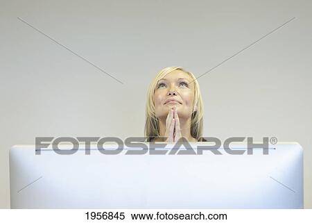 Stock Photography - a young woman looks upwards with praying hands in front of her computer screen; south shields tyne and wear england. Fotosearch