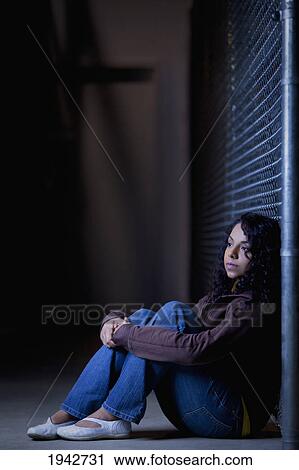 Stock Image - A Young Woman Sits Alone In An Alleyway; Edmonton Alberta Canada. Fotosearch