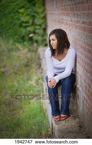 Stock Photo - A Young Woman Sits Along Along A Brick Wall; Edmonton Alberta Canada. Fotosearch