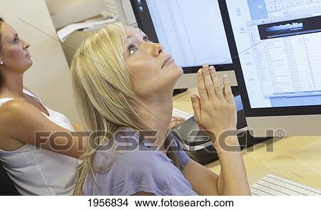 Picture - a young woman sits at her computer at work and looks up with praying hands; south shields tyne and wear england. Fotosearch