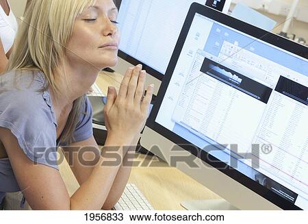 Stock Image - a young woman sits at her computer at work and prays; south shields tyne and wear england. Fotosearch