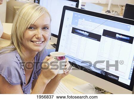 a young woman sits at her work desk in front of her computer holding a coffee mug; south shields tyne and wear england View Large Photo Image Stock Photo - a young woman sits at her work desk in front of her computer holding a coffee mug; south shields tyne and wear england. Fotosearch