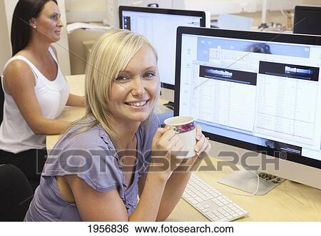 a young woman sits at her work desk in front of her computer holding a coffee mug; south shields tyne and wear england View Large Photo Image Stock Photograph - a young woman sits at her work desk in front of her computer holding a coffee mug; south shields tyne and wear england. Fotosearch