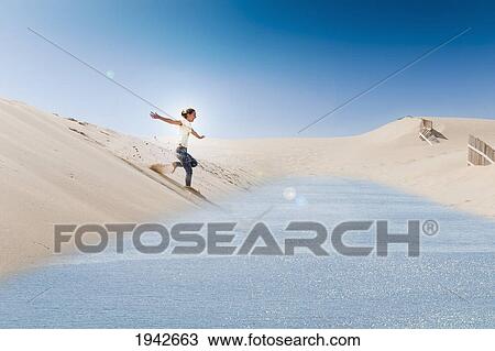 Stock Image - A Young Woman Slides On A Board Over The Punta Paloma Sand Dunes Into The Water; Tarifa Cadiz Andalusia Spain. Fotosearch