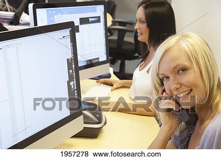 a young woman talks on the phone in front of her computer at her desk; south shields tyne and wear england View Large Photo Image Stock Photo - a young woman talks on the phone in front of her computer at her desk; south shields tyne and wear england. Fotosearch