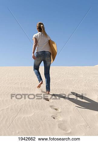 Stock Image - A Young Woman Walks With A Board Over The Punta Paloma Sand Dunes; Tarifa Cadiz Andalusia Spain. Fotosearch